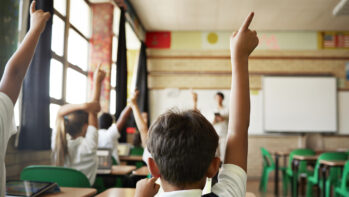 Rear view of boy with raised hand in class