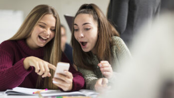 Happy teenage girls in class looking at cell phone